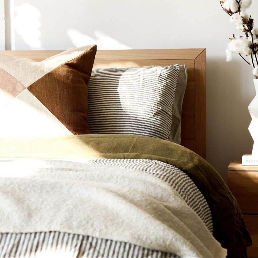 swath of sunlight shines across a well made bed and bedside table with a vase of cotton plants